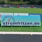 Werbebande mit dem Schriftzug stromfritzen.de am Rasen eines Fußballstadions